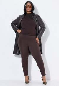 Brun ribbad tröja i kombination med figurnära bruna leggings, lager med en lång svart läderjacka. Tillbehören inkluderar stora bruna solglasögon och mönstrade klackar.