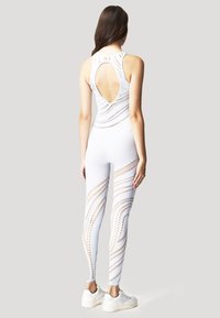 Vit träningsbaddräkt med utskuren rygg, texturerat mönster och meshdetaljer. Figurnära design, kombinerad med vita sneakers.