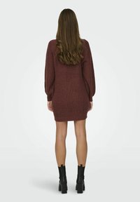 Abito in maglia bordeaux con maniche lunghe, texture a costine e design aderente, abbinato a stivali neri con tacco spesso.