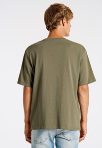 Olivgrön t-shirt med kort ärm, rak skärning, mjukt material och rundad halsringning, kombinerad med ljusblå jeans.