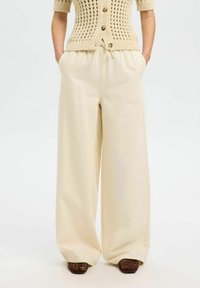 Pantalons larges couleur crème avec une taille élastique, confectionnés en tissu doux. Présente des poches latérales et une coupe décontractée pour le confort.