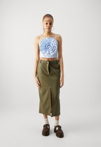 Svetlomodrý crop top s 3D kvetinovým dizajnom, v kombinácii s priliehavou olivovo zelenou sukňou so štrbinou vpredu. Hnedé platformové topánky.