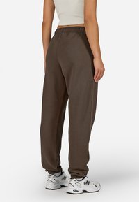 Brūni, brīvi pieguļoši treniņbikši ar elastīgu jostu un piegrieztām potītēm, pārī ar baltām sporta kurpēm. Gluda tekstūra, ikdienišķs dizains.