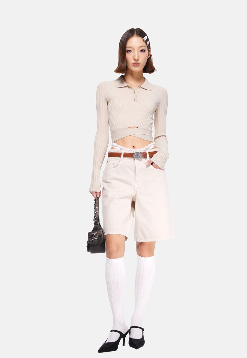 Beige ribbad långärmad topp, högmidjade vita shorts, svarta klackpump, knähöga vita strumpor, brun bälte med silverspänne, liten svart handväska.