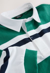 Zeleno-bílé pruhované polo tričko s námořnicky modrými doplňky, vybavené límečkem na knoflíky a texturovanou látkou. Značková etiketa viditelná uvnitř límce.