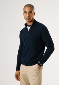 Maglione zip-neck blu navy realizzato in materiale morbido, con maniche lunghe e polsini a coste, caratterizzato da un dettaglio con logo sulla manica sinistra.