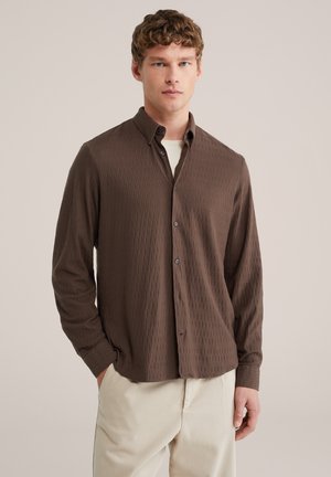 Bruine, geribbelde blouse met knopen, een kraag, lange mouwen en donkere knopen, gecombineerd met lichtgekleurde broek.