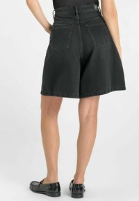 Shorts en denim noir à taille haute, coupe structurée et grandes poches arrière. Les bords sont soigneusement ourlés, créant une silhouette décontractée.