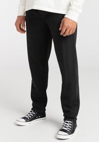 Black sweatpants made of soft material, featuring a tapered design with elastic cuffs. Worn with black high-top sneakers with white accents.