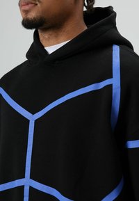 Zwarte hoodie met blauwe geometrische lijnen over de stof. Het materiaal lijkt zacht, met een comfortabele pasvorm en een capuchon met trekkoord.
