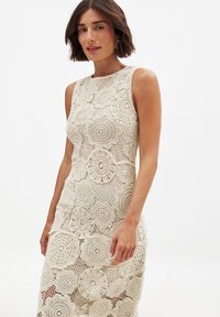 Lace dress in cream with floral crochet patterns, sleeveless design, fitted silhouette, and a round neckline. Textured fabric with intricate detailing.