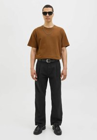 Camisa texturizada de manga corta marrón, pantalones anchos negros, collar de cadena plateada, gafas de sol negras y zapatos negros.