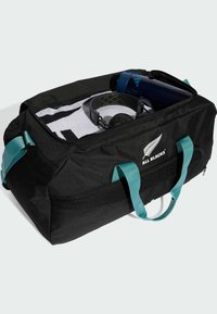 Sort duffelbag med teal håndtag, som har en lynlås på toppen. Indvendigt rummer den et hvidt håndklæde, en vandflaske og hovedtelefoner. Åndbar mesh-sidepanel.
