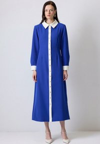 Blue dress with a white collar and placket, long sleeves, featuring gold buttons. Textured fabric with a straight fit down to the ankles.