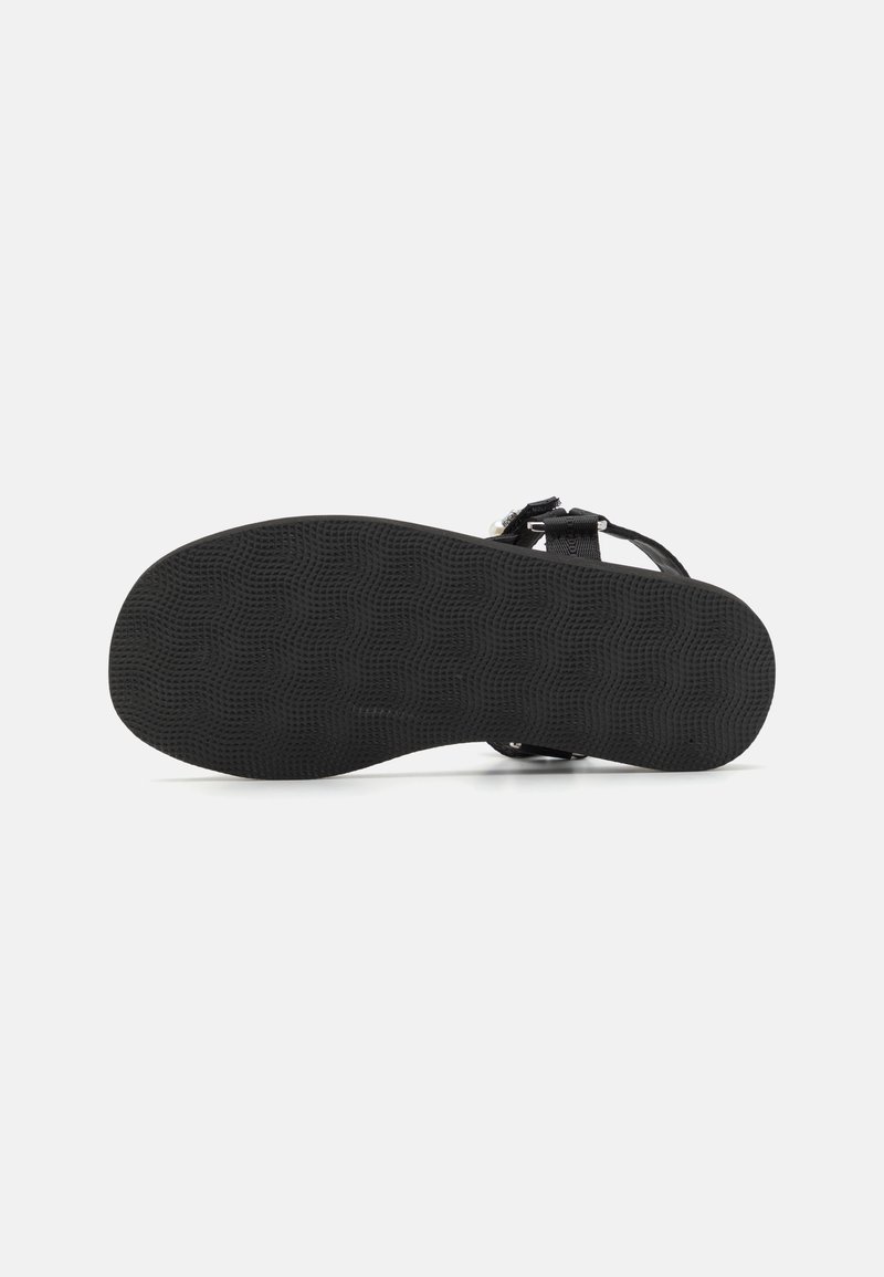 Semelle de sandale noire avec motif de grip texturé. Sangles ajustables avec quincaillerie métallique. Design plat, sans embellissements, style minimaliste.