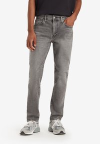Gray denim jeans with a straight cut, five pockets, and a relaxed fit. Worn with gray and white sneakers.