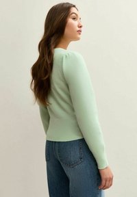 Suéter verde menta hecho de material suave, con un dobladillo acanalado y mangas abullonadas. Combinado con jeans de talle alto.