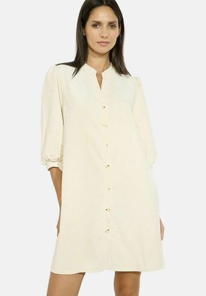 Robe beige clair avec décolleté en V, fermeture à boutons à l'avant et manches bouffantes; fabriquée dans un tissu doux avec une texture lisse et un éclat subtil.