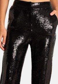 Pantalons noirs en sequins à taille haute, présentant un design ajusté et des poches latérales. Le tissu a une surface brillante et texturée.