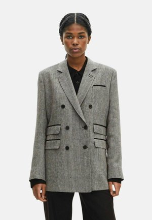 Blazer de doble botonadura en tela de espiga gris, con botones negros, bolsillos laterales y solapas en pico. Ajuste texturizado y entallado.
