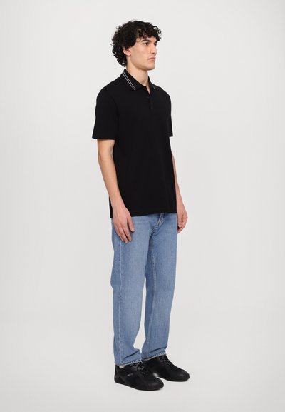 Svart pikétröja med randig krage, kombinerad med ljusblå jeans och svarta sneakers. Tröjan har en avslappnad passform och korta ärmar.