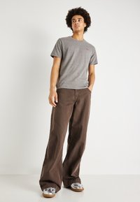 Camiseta de algodón gris con mangas cortas, combinada con pantalones de mezclilla marrones de corte holgado y zapatillas plateadas con un patrón texturizado.