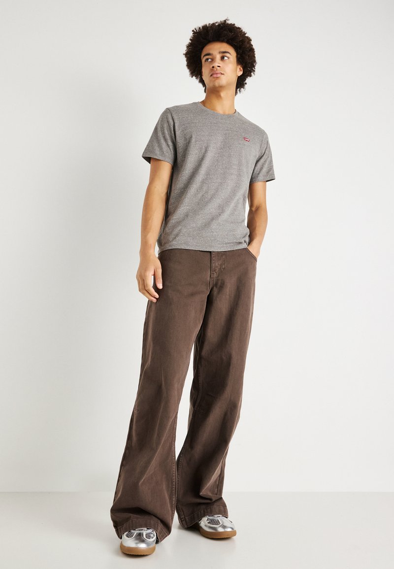 Szara bawełniana koszulka z krótkimi rękawami, w połączeniu z luźnymi brązowymi dżinsami i srebrnymi sneakerami o teksturowanym wzorze.