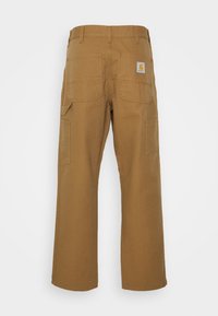 Carhartt work pants in a solid tan color, featuring a straight-leg cut, multiple pockets, and a logo patch on the back right. Durable fabric.