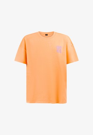 Pomarańczowa koszulka z krótkim rękawem i okrągłym dekoltem, z małą fioletową abstrakcyjną grafiką na lewej górnej części klatki piersiowej.