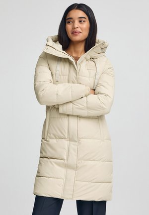 Beige donsjas met capuchon. Voorzien van een doorgestikt ontwerp, een ritssluiting aan de voorkant en twee zijzakken. "Polo Club" logo met een gestructureerde afwerking.