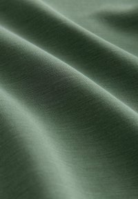 La tela verde presenta una superficie suave y ligeramente texturizada con arrugas y pliegues sutiles, destacando un material suave y elástico.