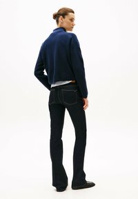  granatowy sweter z dzianiny o kroju cropped, zestawiony z ciemnoniebieskimi spodniami dzwonami. Ubranie ma klasyczne szwy i tylne kieszenie.