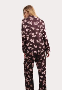 Lila Satin-Pyjama-Set mit einem floralen Muster in hellrosa. Enthält ein Hemd mit Kragen und passende Hosen, mit langen Ärmeln und einem lockeren Schnitt.