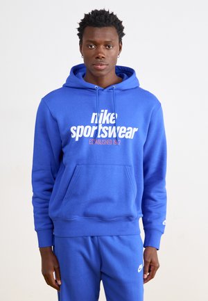 Blue hoodie made of soft fabric with a kangaroo pocket. Features a white logo and text design on the front. Paired with matching blue pants.