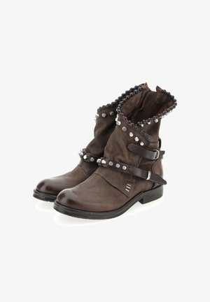 Braune Lederknöchelstiefel mit schwarzen Perlen und silbernen Nieten, die über Riemen und Schnallen verfügen, vor einem weißen Hintergrund.