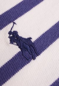 Bílá bavlněná látka s vodorovnými námořnickými proužky. Obsahuje vyšívané logo námořnického jezdce na proužku. Hladká textura.