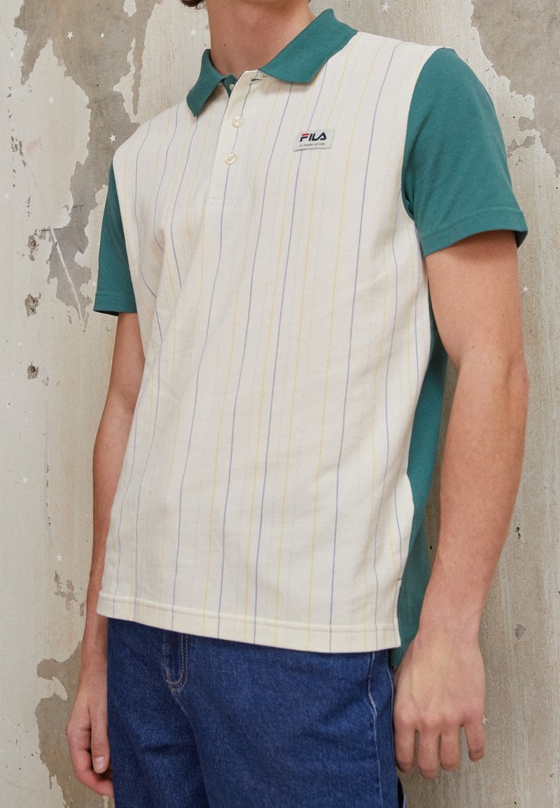 Polo-shirt à rayures blanches avec des manches courtes et un col vert, présentant des rayures verticales jaunes et bleues, ainsi qu'un petit logo sur la poitrine.