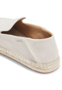 Lichtbeige suède espadrille met gevlochten jutezool en subtiel geperst "BOSS"-logo aan de zijkant, weergegeven vanuit een close-up achteraanzicht.