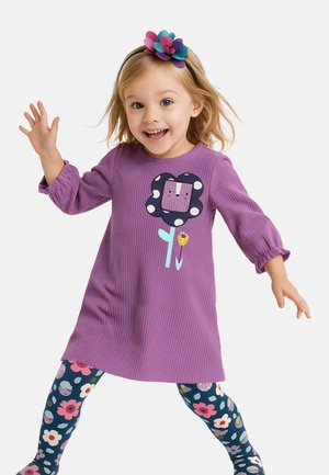 Robe violette à côtes avec une appliqué fleurie ornée de pois. Associée à des leggings à motifs floraux colorés et un bandeau à fleurs multicolores.
