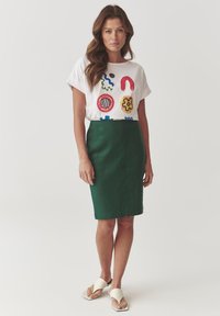 Un tricou alb cu modele abstracte colorate, asortat cu o fustă conică verde închis. Modelul poartă sandale albe cu vârf deschis și toc pătrat.