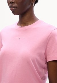 Lyserød bomulds T-shirt med korte ærmer og rund hals. Har "TOMMY JEANS" logoet trykt på brystet i hvid. Glat tekstur.
