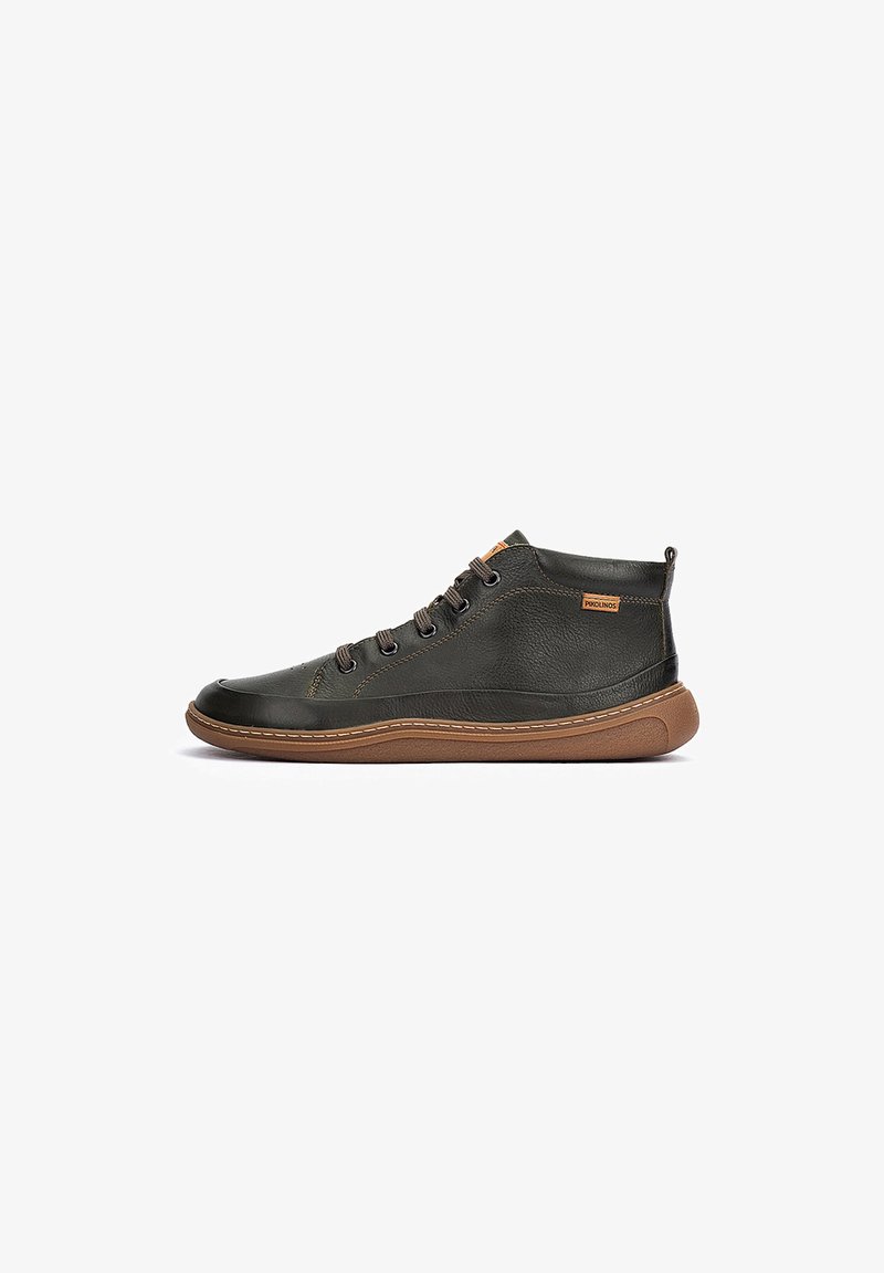 Zapatillas de media bota en cuero verde oscuro con suelas de goma marrón, que cuentan con ojales de metal y un sistema de cordones simplificado para un ajuste seguro.