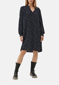 Robe fleurie bleu marine à manches longues, avec un décolleté en V et des détails smockés. Assortie à des bottes noires jusqu'aux genoux avec une semelle épaisse.