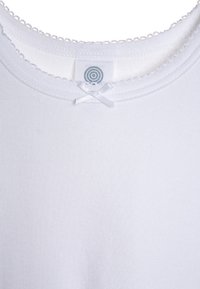T-shirt bianco in cotone con scollatura rotonda, piccolo dettaglio con fiocco in raso e delicata rifinitura in pizzo lungo il colletto.