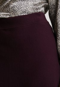 Hög midja burgunderfärgad kjol med ribbad textur. Kombinerad med en beige topp med ett svart leopardmönster.