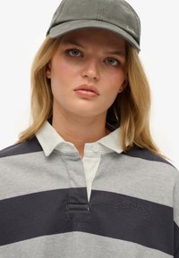 Langärmliges Rugby-Shirt in grauen und marineblauen Streifen, mit einem weißen Kragen und einer knöpfbaren Blende, auf der "Superdry" auf der Brust gestickt ist.