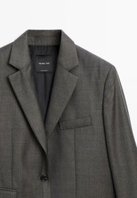 Gray blazer made of textured fabric. Features a notched collar, single button closure, and a chest pocket for added detail.