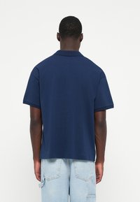 Mörkblå pikétröja i bomull med korta ärmar och avslappnad passform. Slät yta med klassisk krage och utan synlig branding.