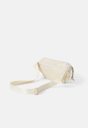 Lille cremefarvet kordurov crossbody-taske med justerbar rem og lynlåslukning på en ensfarvet hvid baggrund.
