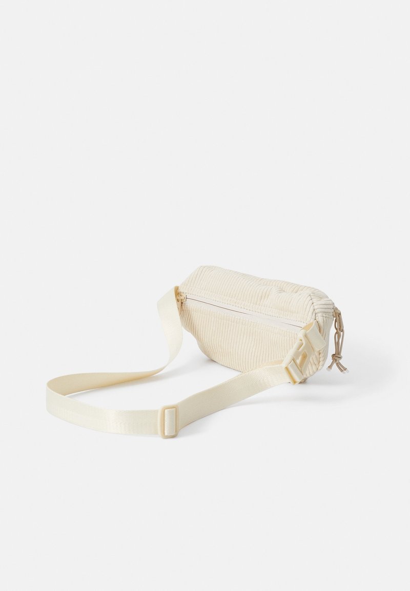 Petit sac bandoulière en velours côtelé crème avec sangle réglable et fermeture éclair sur fond blanc uni.